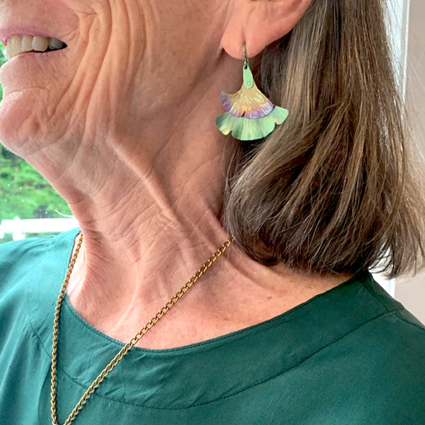 Close-up of a person wearing colorful gingko leaf earrings.
