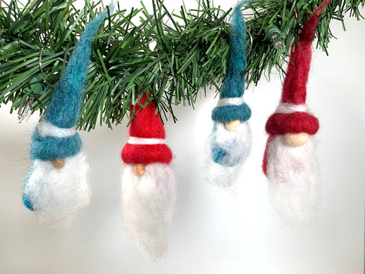 Four felted gnome ornaments with red and blue hats hanging from a Christmas tree.